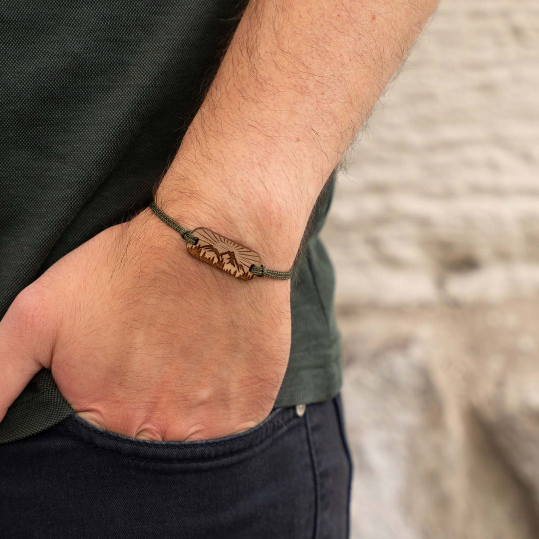 Nussbaum-Armband mit Naturgravur – Berge, Wald und Sonne als filigranes Motiv mit olivgrünem Nylonband